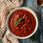 White bowl with sugo and basil, crushed red pepper in small bowl.