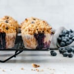 Buttermilk blueberry muffins with streusel topping on a cooling rack with blueberries on side.