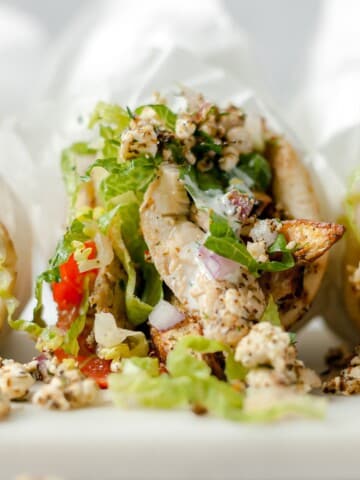 Closeup of chicken pita wrapped in parchment with lettuce, tomato, onion and feta cheese.