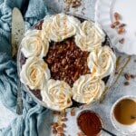 Whole turtle pie with whipped cream, a spatula, chocolate ganache bowl and bowl of caramel.