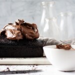 Chocolate loaf cake, sour cream fudge frosting, white bowl and glasses in the background