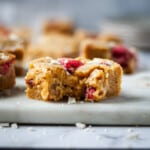 Square of white chocolate raspberry blondies with a bite taken out of one.