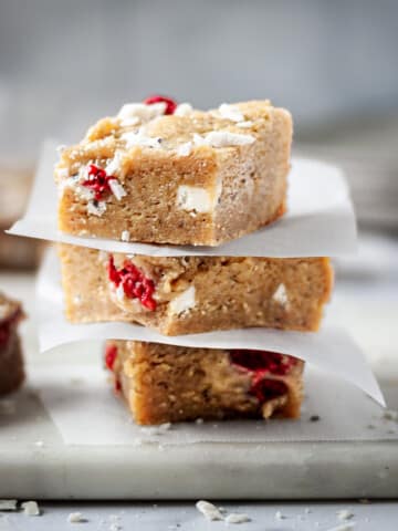 stacked white chocolate raspberry blondies with parchment paper between.