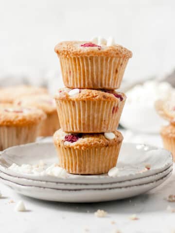 Stack of raspberry and white chocolate muffins on a plate with other muffins in the background.